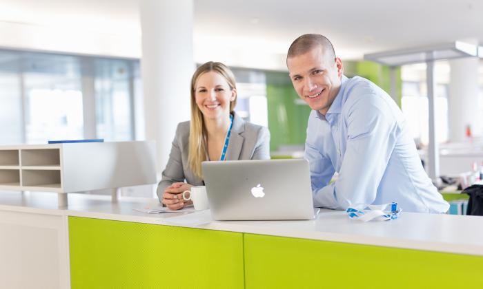 A female and a male graduate smiling at the Uniper office with a laptop