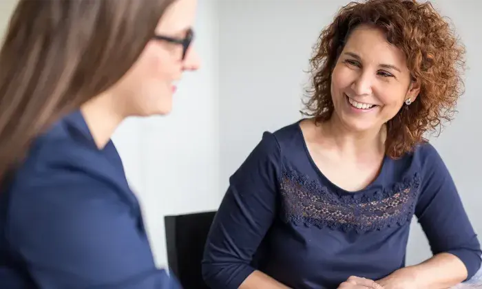 Two women sitting at a table, smiling and engaging in conversation during a professional meeting.