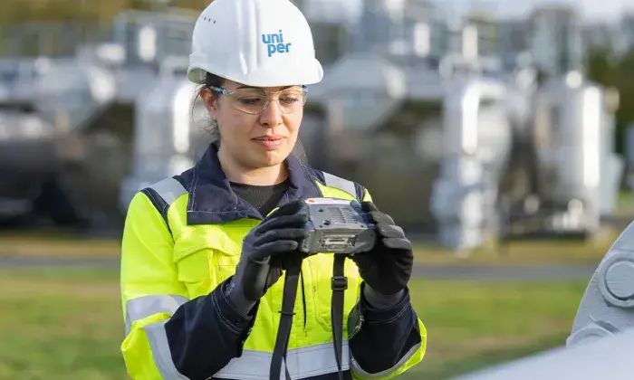 A Uniper worker in high-visibility clothing and a safety helmet inspecting equipment outdoors at an industrial facility