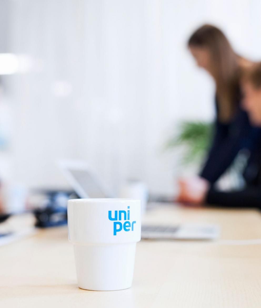 Uniper Tasse steht auf einem Besprechnungstisch, im Hintergrund sind drei Mitarbeiterinnen zu sehen