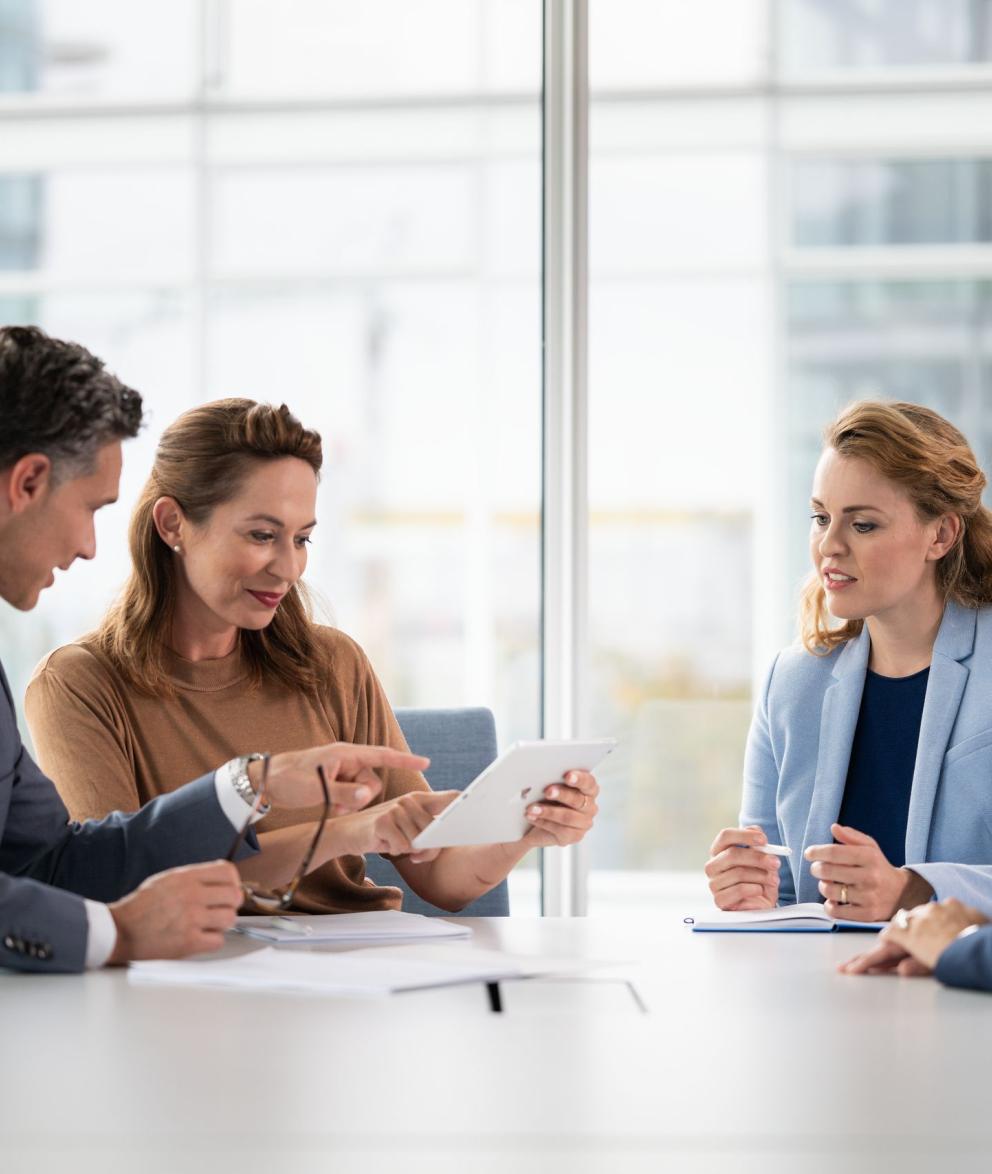 Ein Mann und drei Frauen in Business Kleidung sitzen in einem Besprechungsraum und reden miteinander