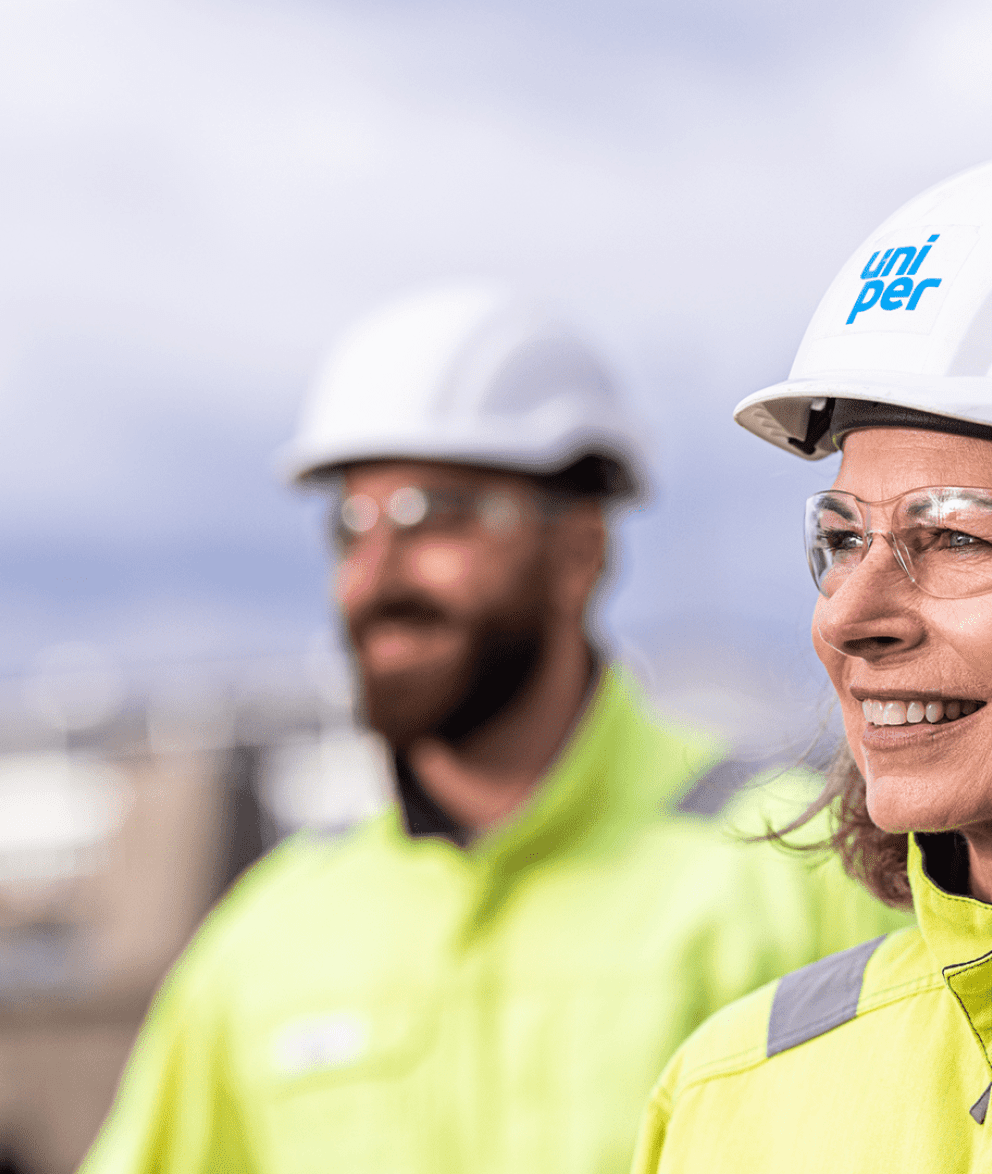 Eine weibliche und ein männlicher Uniper Mitarbeiter:in im Hintergrund mit Helmen und Sicherheitsbrille