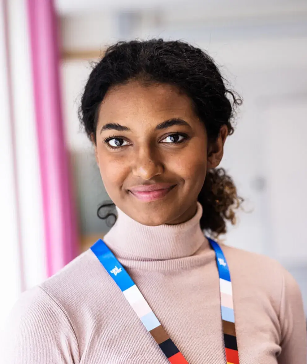 Smiling Uniper employee wearing a colorful lanyard, standing in a modern office environment with a soft, neutral background.