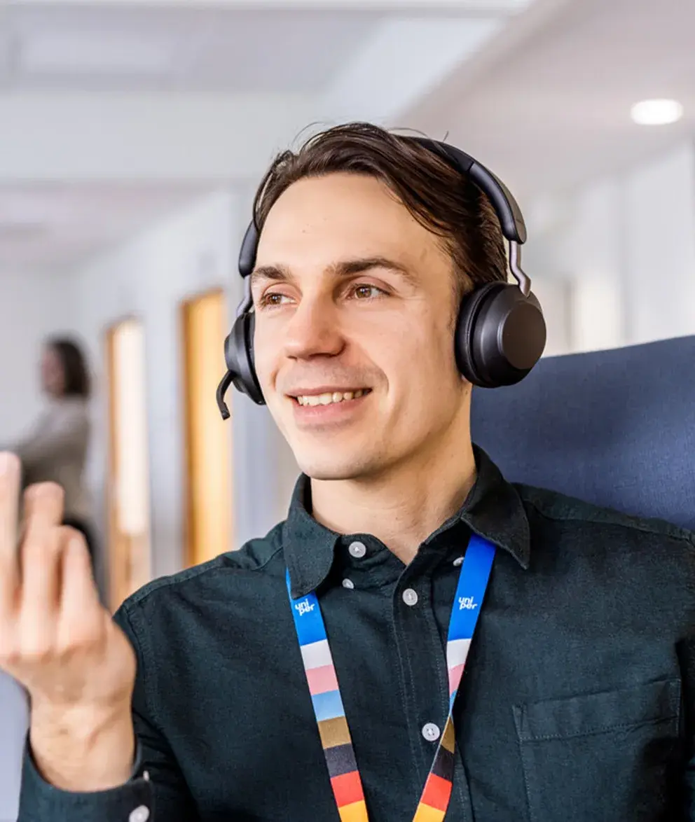 A smiling Uniper employee wearing headphones and a colorful lanyard, engaged in a conversation or virtual meeting, in a modern office environment.