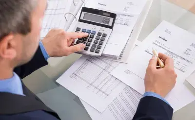 Business professional using a calculator to review financial documents and invoices at a desk