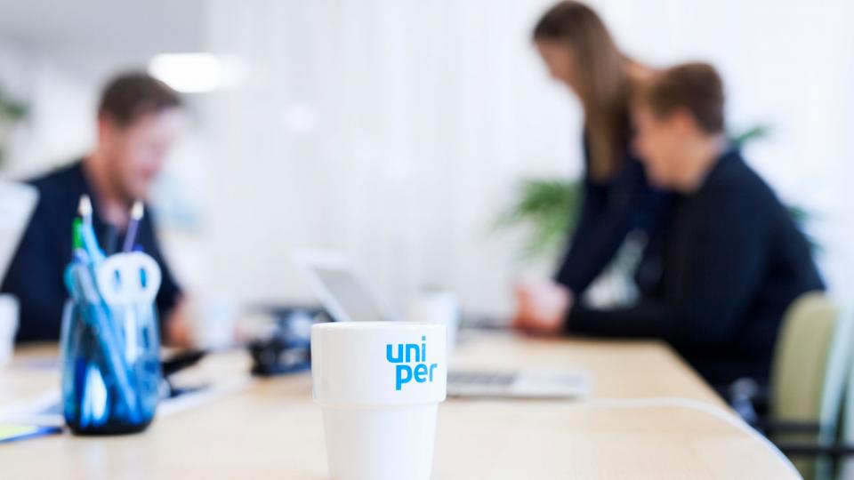 Uniper Tasse steht auf einem Besprechnungstisch, im Hintergrund sind drei Mitarbeiterinnen zu sehen