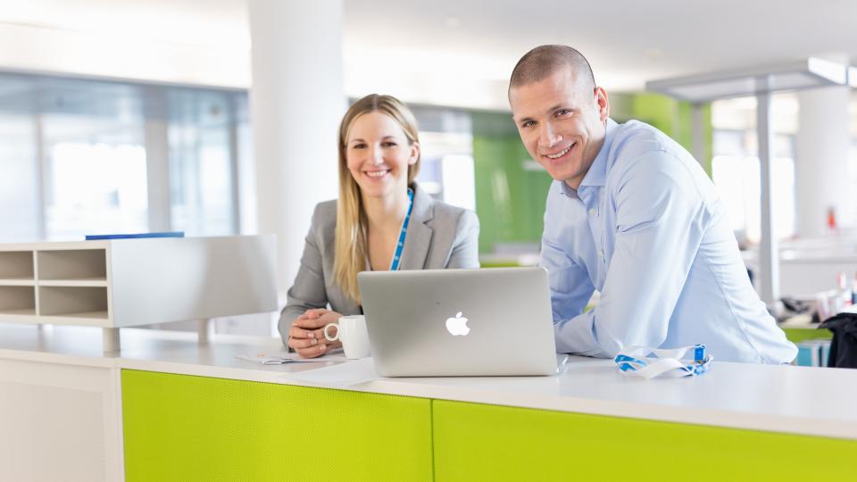 Weibliche und männlicher Uniper-Mitarbeiter:in lächelnd in Uniper-Büro mit Laptop