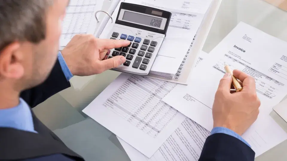 Business professional using a calculator to review financial documents and invoices at a desk