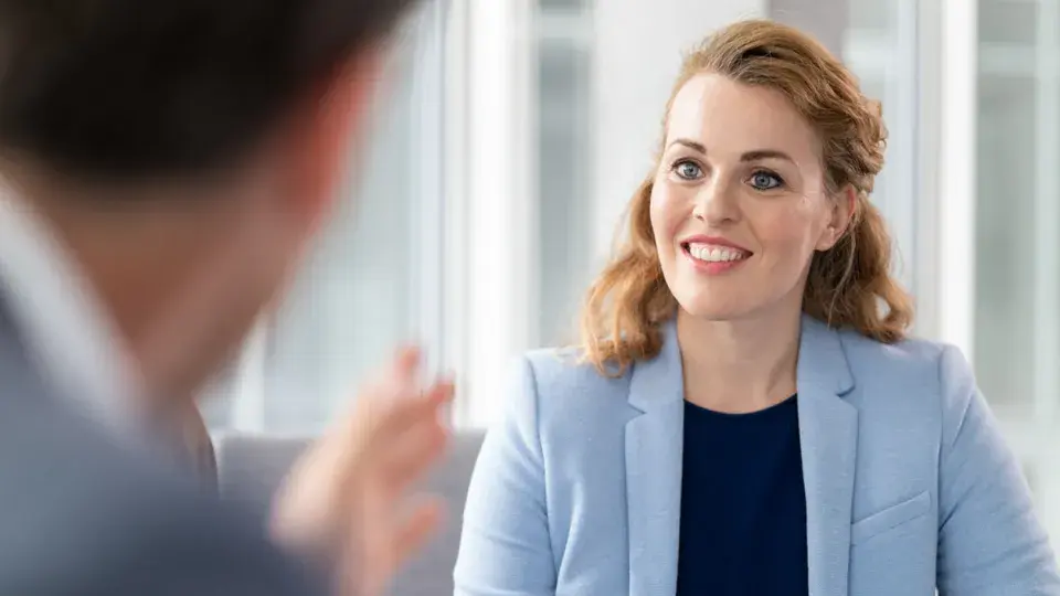Professional woman smiling and listening during a conversation in a modern office setting.