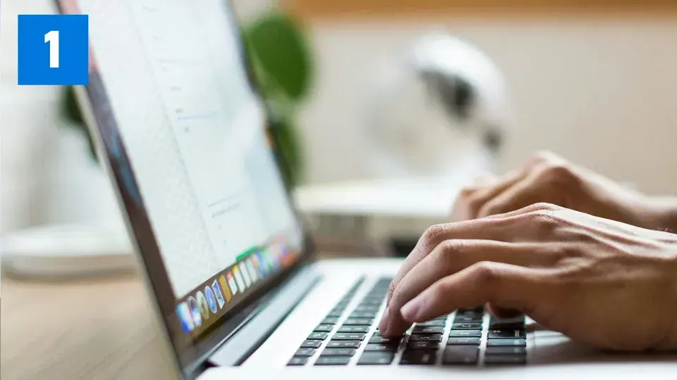 Close-up of hands typing on a laptop keyboard, with a document open on the screen and a blue box with the number '1' in the top left corner.