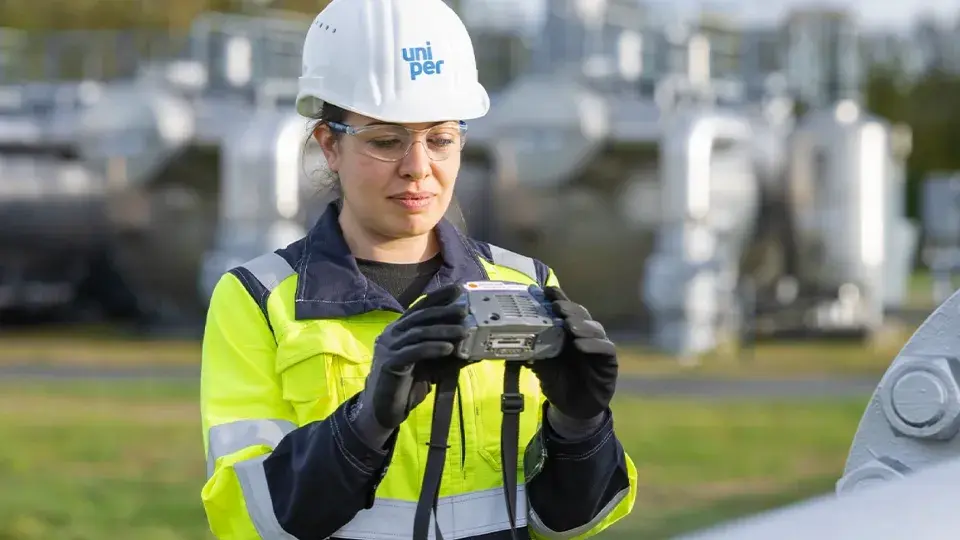 A Uniper worker in high-visibility clothing and a safety helmet inspecting equipment outdoors at an industrial facility