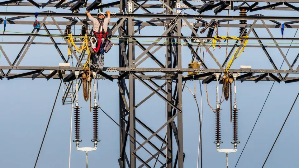 Worker performing maintenance on a high-voltage transmission tower.