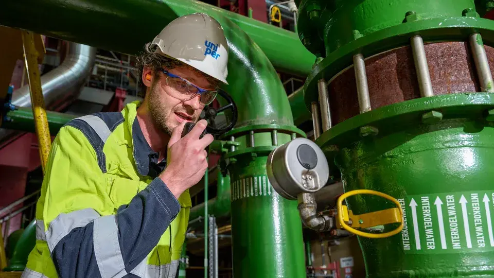 Uniper employee in safety gear communicating via radio in an industrial setting.