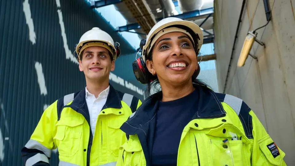 Two Uniper employees in safety gear smiling outdoors at an industrial facility.