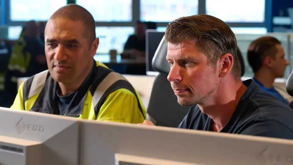 Two workers closely monitoring data on computer screens in a modern control room, representing the product-as-a-service model in action.