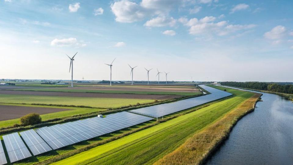 Solar Panels and wind turbines by a river in daylight