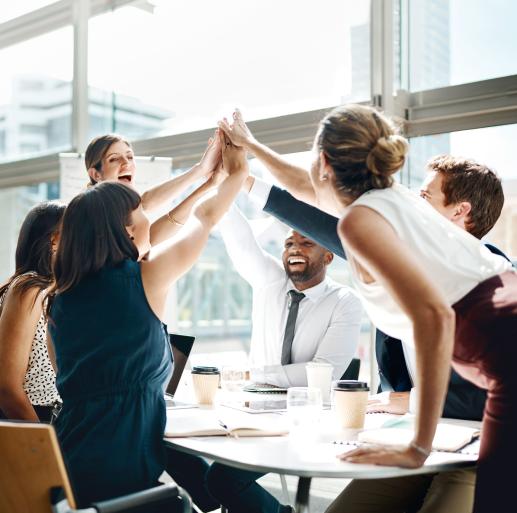 Sechs männliche und weibliche Kolleg:innen freuen sich und klatschen sich bei einer Besprechung im Büro gegenseitig ab