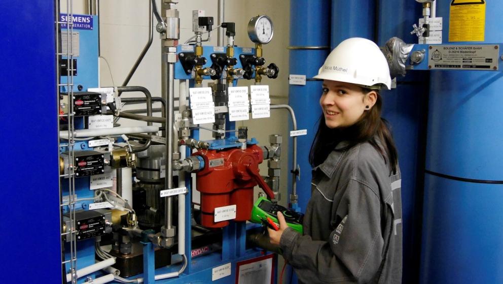 Female apprentice with helmet standing at machine in power plant