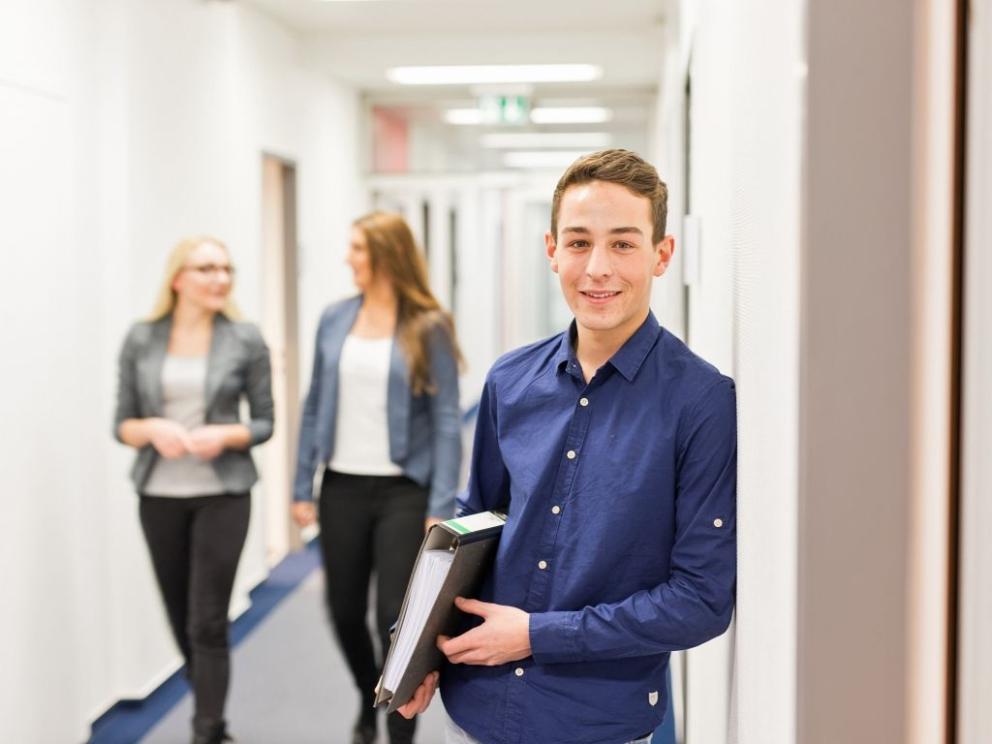 Male Uniper apprentice with a file folder and two female employees in the background