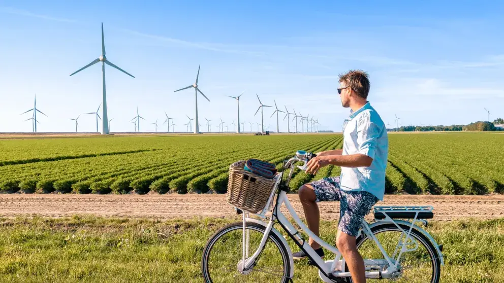 A person on a bicycle in a rural landscape, looking at a field of wind turbines generating renewable energy under a clear blue sky.