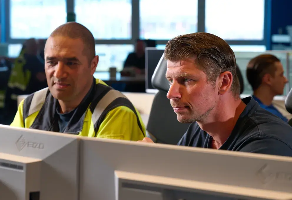 Two workers closely monitoring data on computer screens in a modern control room, representing the product-as-a-service model in action.