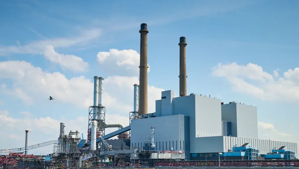 Wide-angle view of the UCML natural gas power plant at Uniper's Maasvlakte Energy Hub, featuring tall chimneys and industrial infrastructure under a partly cloudy sky.
