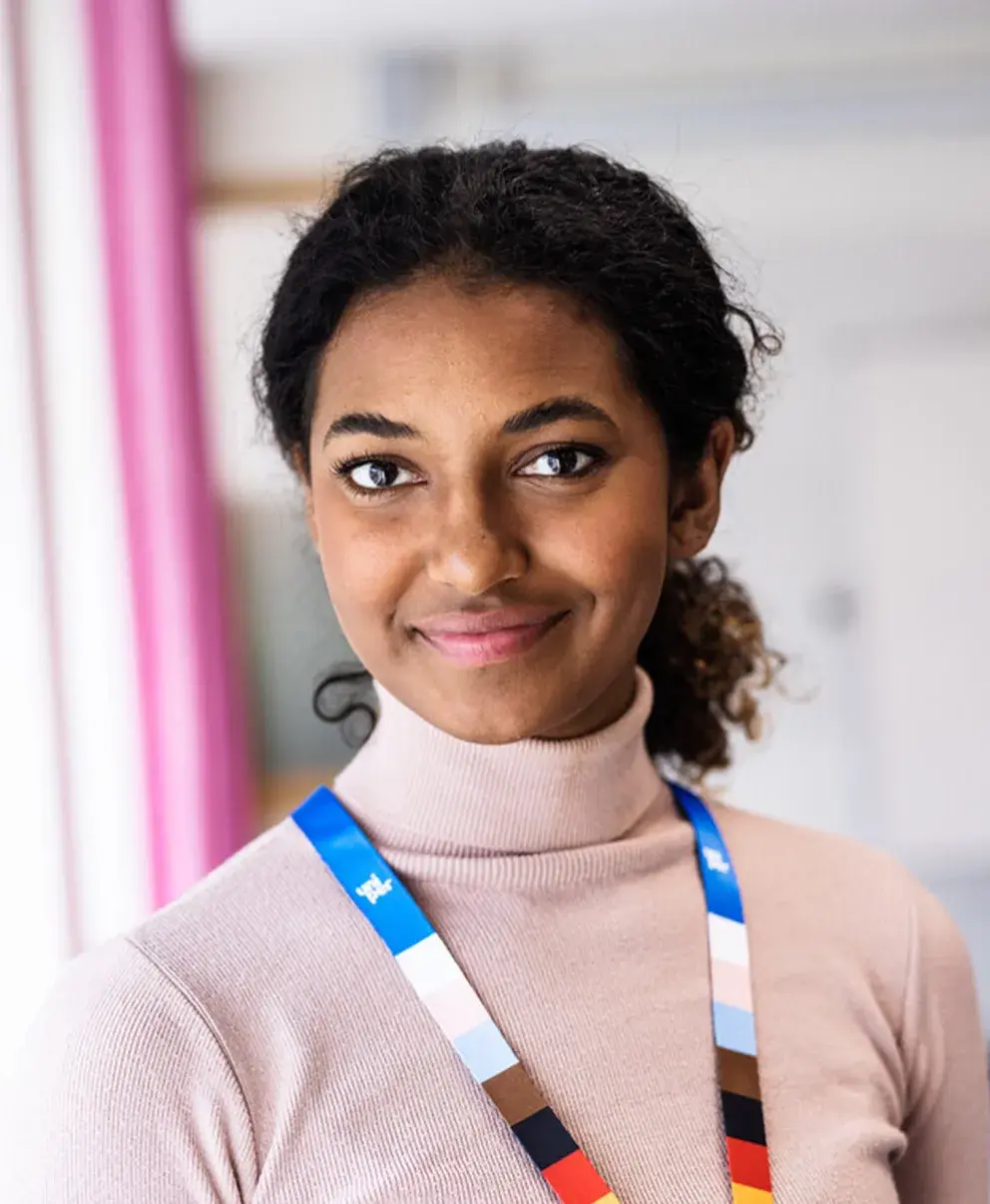 Smiling Uniper employee wearing a colorful lanyard, standing in a modern office environment with a soft, neutral background.