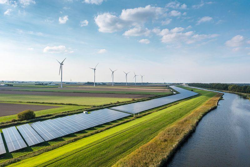 Solar Panels and wind turbines by a river in daylight