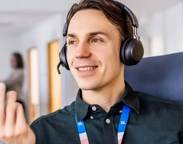 A smiling Uniper employee wearing headphones and a colorful lanyard, engaged in a conversation or virtual meeting, in a modern office environment.